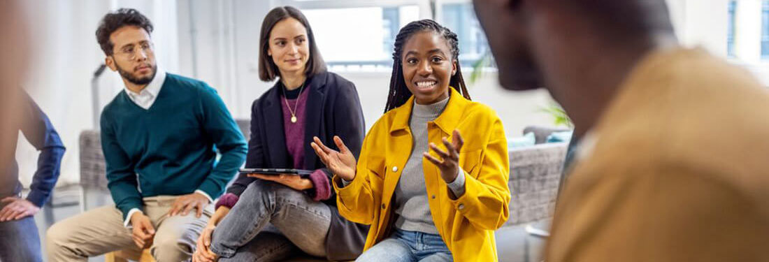 African woman talking with colleagues sitting in circle at a coworking office.