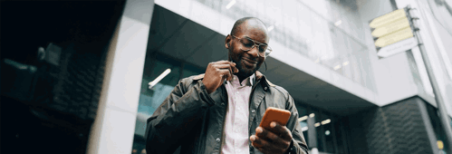 Person outside office building smiling and looking at mobile phone