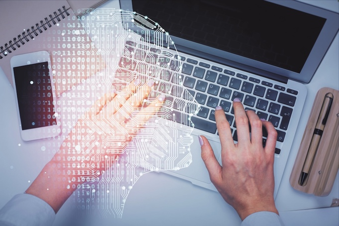A human brain design overlaid a person typing on laptop