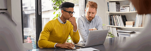Mature and young businessmen discussing during meeting in boardroom. Business executive working with apprentice in creative office. Multiethnic business team in smart casual with partner working together on laptop.