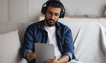 Man wearing headphones using a tablet whilst sat on the sofa