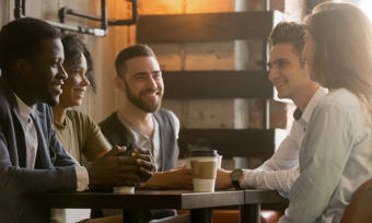 A diverse group of friends engaged in conversation while sitting around a table drinking coffee